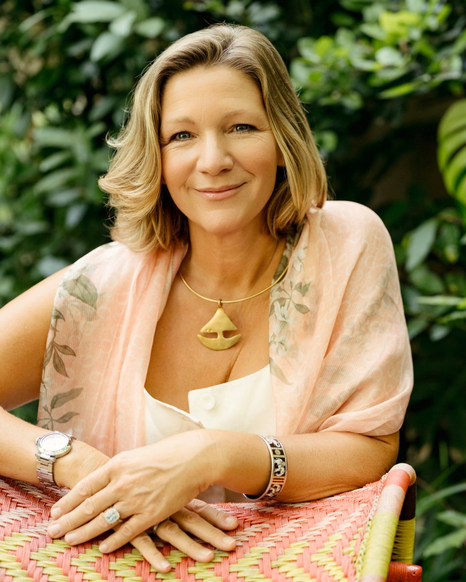 Libby Pickett in a garden, smiling, leaning on the back of a woven chair.